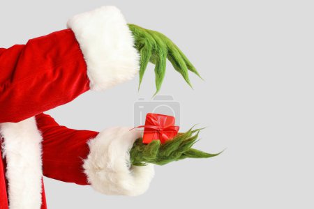 Foto de Verde manos peludas de criatura en traje de Santa con caja de regalo sobre fondo gris - Imagen libre de derechos