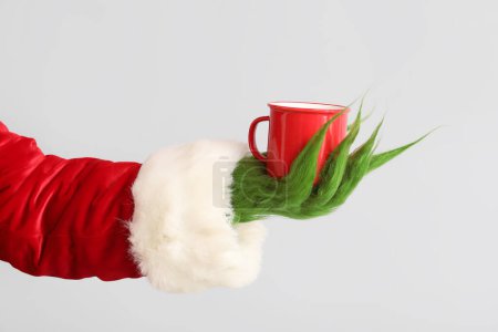 Photo for Green hairy creature in Santa costume with cup of coffee on grey background - Royalty Free Image