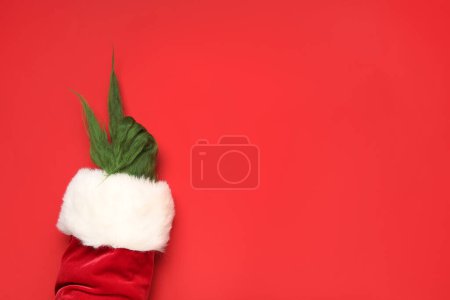 Téléchargez les photos : Poilu main de créature verte en costume de Père Noël pointant quelque chose sur fond rouge - en image libre de droit