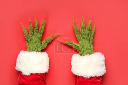 Téléchargez les photos : Mains poilues de créature verte en costume de Père Noël sur fond rouge - en image libre de droit