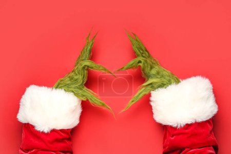 Téléchargez les photos : Mains poilues vertes de créature en costume de Père Noël montrant geste de coeur sur fond rouge - en image libre de droit
