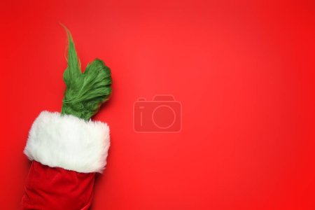 Téléchargez les photos : Main poilue verte de créature en costume de Père Noël montrant geste pouce vers le haut sur fond rouge - en image libre de droit