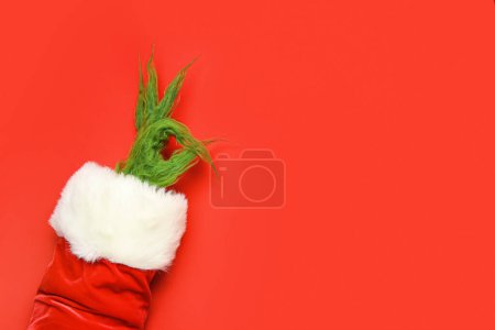 Téléchargez les photos : Main poilue verte de créature en costume de Père Noël montrant OK geste sur fond rouge - en image libre de droit