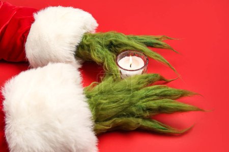 Foto de Verde manos peludas de criatura en traje de Santa con vela sobre fondo rojo - Imagen libre de derechos