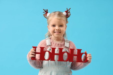 Téléchargez les photos : Petite fille mignonne avec des oreilles de rennes et salutation de Noël sur fond bleu - en image libre de droit