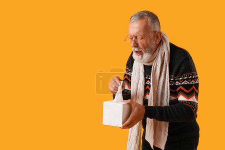 Téléchargez les photos : Malade homme mûr avec boîte de tissu éternuer sur fond jaune - en image libre de droit