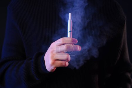 Téléchargez les photos : Jeune homme avec cigarette électronique sur fond noir, gros plan - en image libre de droit