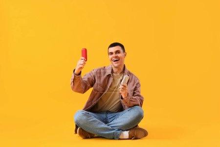 Téléchargez les photos : Jeune homme avec des cigarettes électroniques sur fond jaune - en image libre de droit