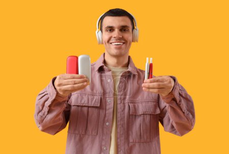 Téléchargez les photos : Jeune homme avec cigarettes électroniques et écouteurs sur fond jaune - en image libre de droit