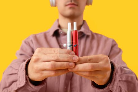 Téléchargez les photos : Jeune homme avec des cigarettes électroniques sur fond jaune, gros plan - en image libre de droit