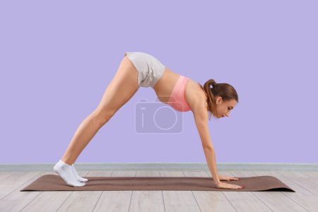 Foto de Mujer joven haciendo yoga contra la pared lila - Imagen libre de derechos