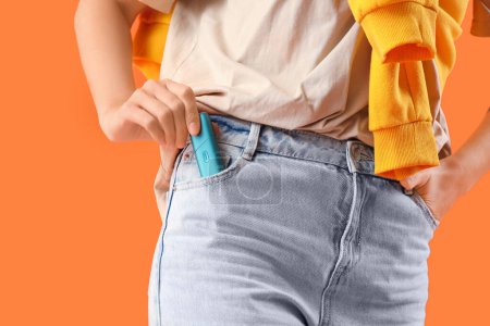 Téléchargez les photos : Jeune femme avec cigare électronique dans la poche du jean sur fond orange, gros plan - en image libre de droit