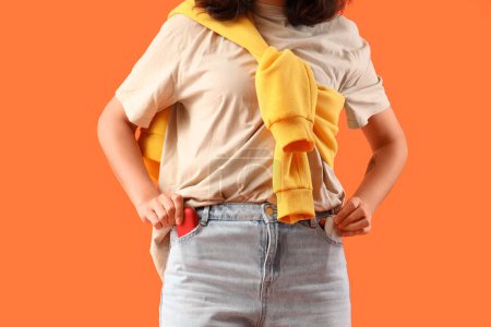 Téléchargez les photos : Jeune femme avec bloc de cigare électronique dans la poche du jean sur fond orange, gros plan - en image libre de droit