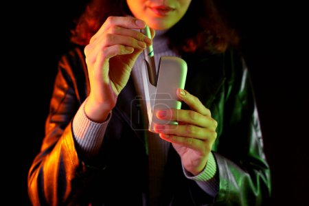 Téléchargez les photos : Jeune femme avec bloc de cigare électronique sur fond sombre, gros plan - en image libre de droit