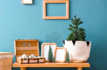 Photo for Wooden bench with blank frames, mini Christmas trees and baubles in suitcase near blue wall - Royalty Free Image