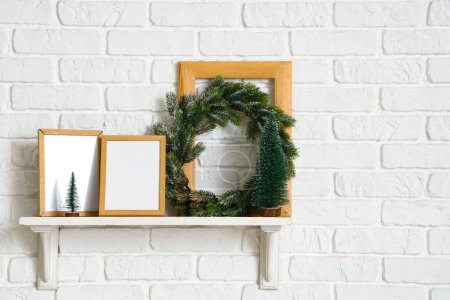 Photo for Shelf with blank photo frames and Christmas wreath hanging on white brick wall - Royalty Free Image