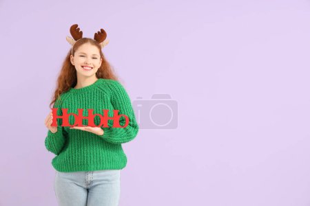 Téléchargez les photos : Jeune femme en cornes de rennes avec salutation de Noël sur fond lilas - en image libre de droit