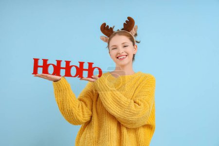Téléchargez les photos : Jeune femme en cornes de rennes avec salutation de Noël sur fond bleu - en image libre de droit