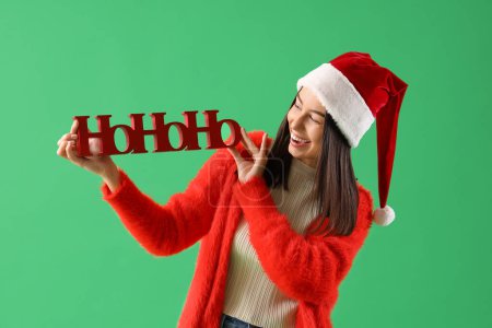 Téléchargez les photos : Jeune femme en chapeau de Père Noël avec salutation de Noël sur fond vert - en image libre de droit
