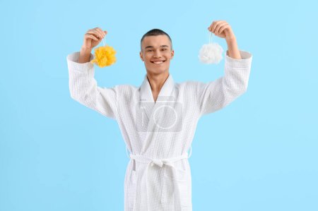 Teenage boy in bathrobe with loofahs on blue background