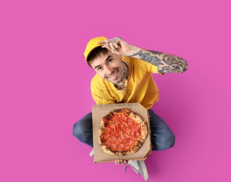 Photo for Handsome tattooed young man with tasty pizza sitting on purple background - Royalty Free Image