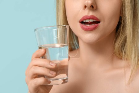 Photo for Young woman with vitamin A pill and glass of water on blue background, closeup - Royalty Free Image