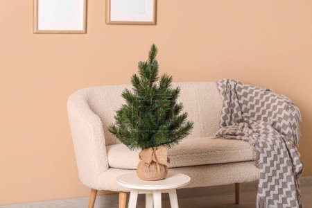 Photo for Small Christmas tree on stool with sofa near beige wall - Royalty Free Image