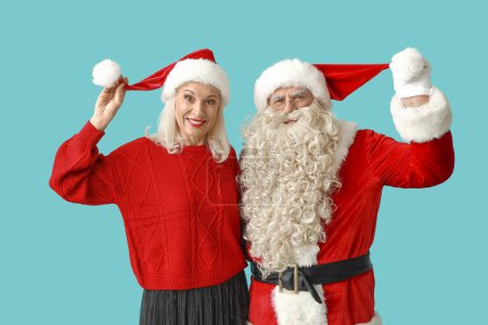 Téléchargez les photos : Joyeux Père Noël et belle femme mature dans des chapeaux de Noël sur fond bleu - en image libre de droit