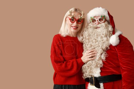 Téléchargez les photos : Joyeux Père Noël et belle femme mature dans des lunettes de Noël sur fond brun - en image libre de droit