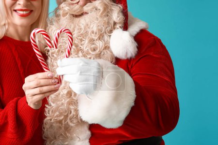 Téléchargez les photos : Père Noël et belle femme mature avec des cannes de bonbons sur fond bleu, gros plan - en image libre de droit