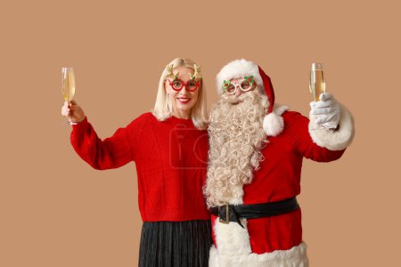 Téléchargez les photos : Joyeux Père Noël et belle femme mûre dans des verres de Noël avec des verres de champagne sur fond brun - en image libre de droit