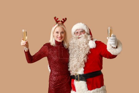 Téléchargez les photos : Père Noël et belle femme mûre dans des cornes de cerf de Noël avec des verres de champagne sur fond brun - en image libre de droit