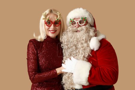 Téléchargez les photos : Père Noël et belle femme mature dans des lunettes de Noël sur fond brun - en image libre de droit