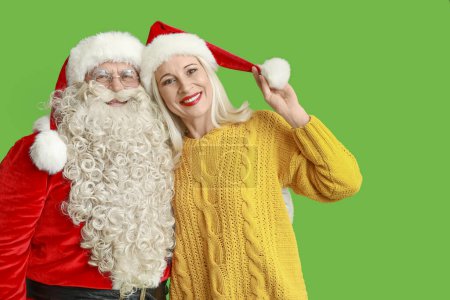 Téléchargez les photos : Père Noël et belle femme mature dans des chapeaux de Noël sur fond vert - en image libre de droit