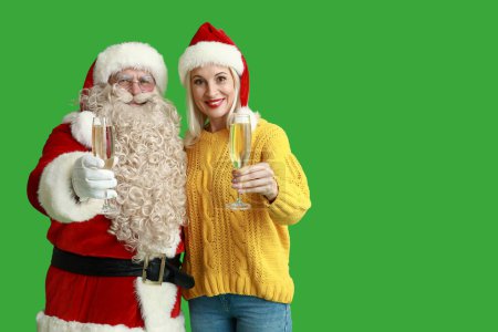 Téléchargez les photos : Père Noël et belle femme mature dans des chapeaux de Noël avec des verres de champagne sur fond vert - en image libre de droit