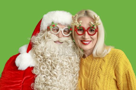Téléchargez les photos : Père Noël et belle femme mature dans des lunettes de Noël sur fond vert - en image libre de droit