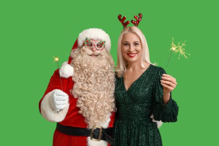 Téléchargez les photos : Père Noël et belle femme mûre dans les cornes de cerf de Noël avec des étincelles sur fond vert - en image libre de droit