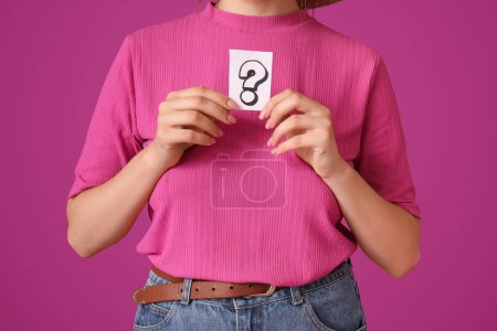 Photo for Thoughtful young woman holding paper sheet with question mark on purple background - Royalty Free Image