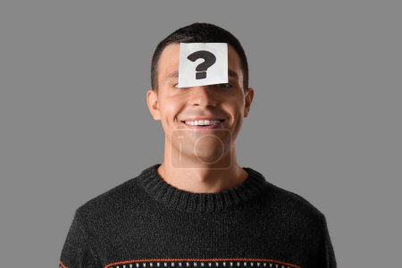 Photo for Young man with paper question mark on his forehead against grey background - Royalty Free Image