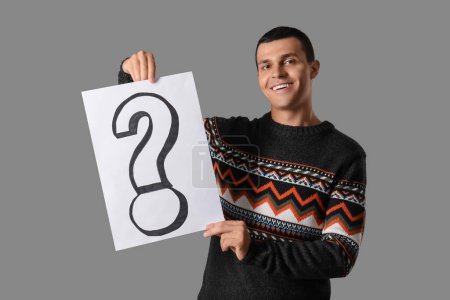 Photo for Young man holding paper with question mark on grey background - Royalty Free Image