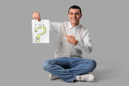 Photo for Young man pointing at paper with question mark on grey background - Royalty Free Image