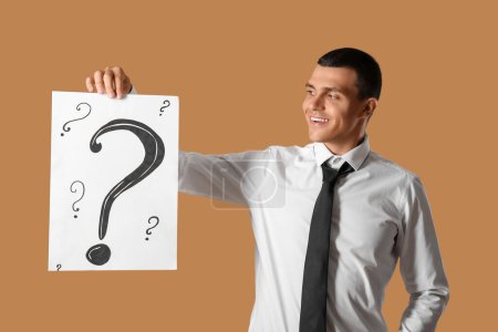 Photo for Young man holding paper with question marks on brown background - Royalty Free Image