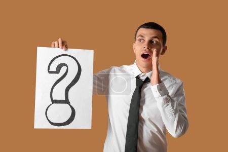 Photo for Shocked young man holding paper with question mark on brown background - Royalty Free Image
