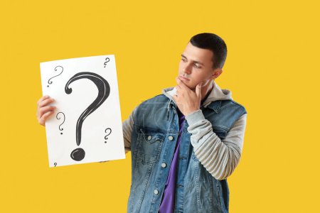 Photo for Wondering young man holding paper with question marks on yellow background - Royalty Free Image