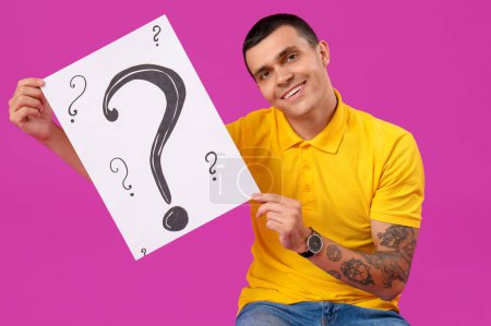 Photo for Young man holding paper with question marks on purple background - Royalty Free Image