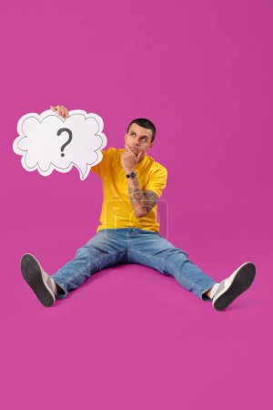 Photo for Wondering young man holding speech bubble with question mark on purple background - Royalty Free Image