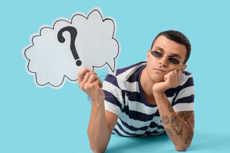 Photo for Young man holding paper with question mark on blue background - Royalty Free Image