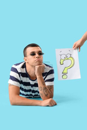 Photo for Young man and paper with question mark on blue background - Royalty Free Image