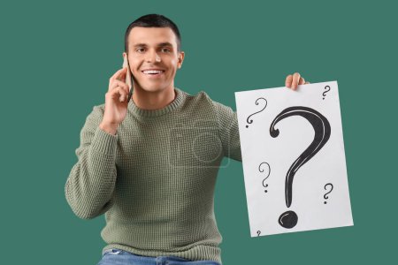 Photo for Young man with paper question marks talking by mobile phone on green background - Royalty Free Image