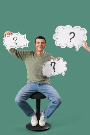 Photo for Young man holding speech bubbles with question marks on green background - Royalty Free Image